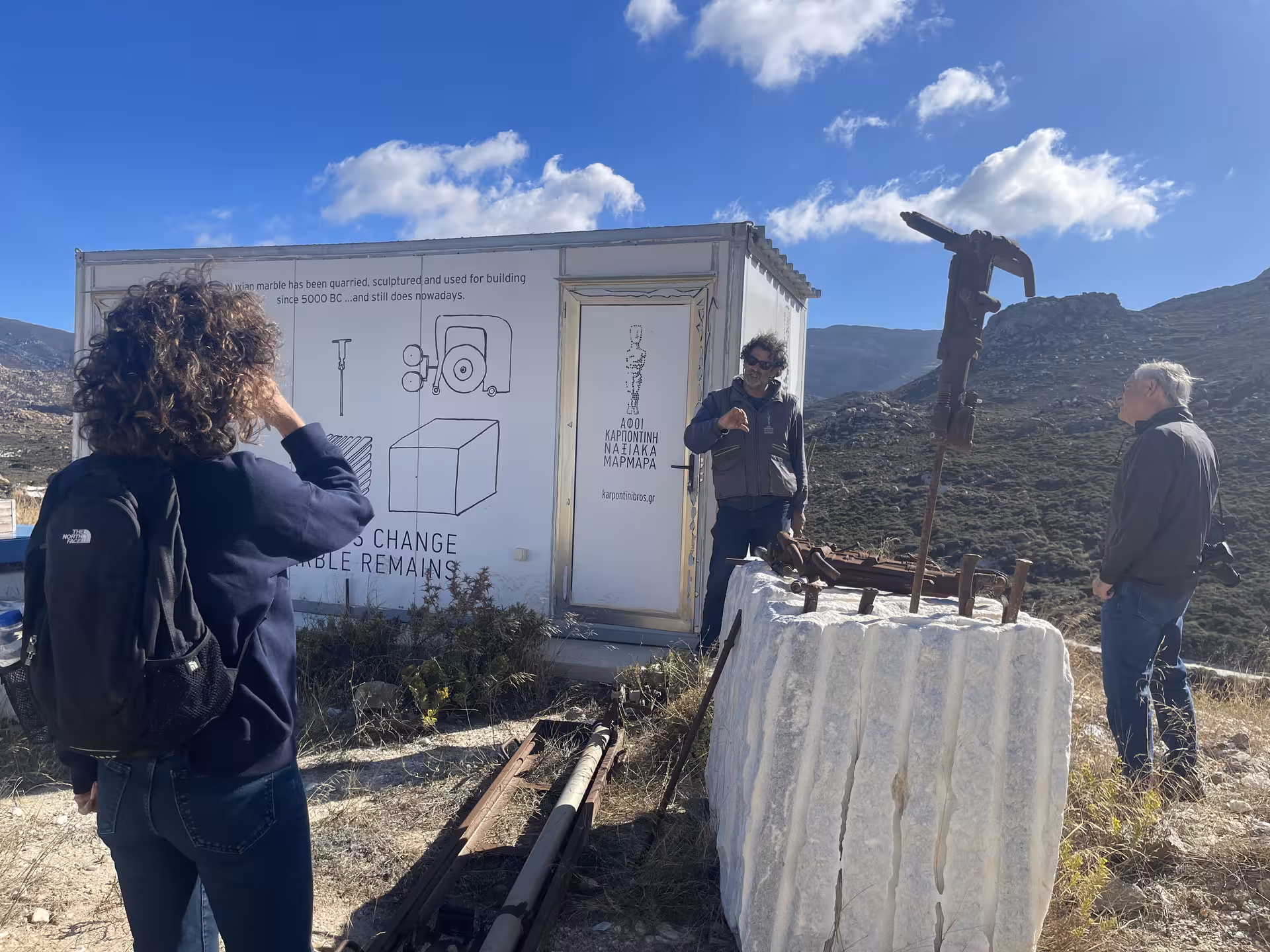 Marble World tour guide explains traditional quarry tools beside a raw marble block in the Greek mountains