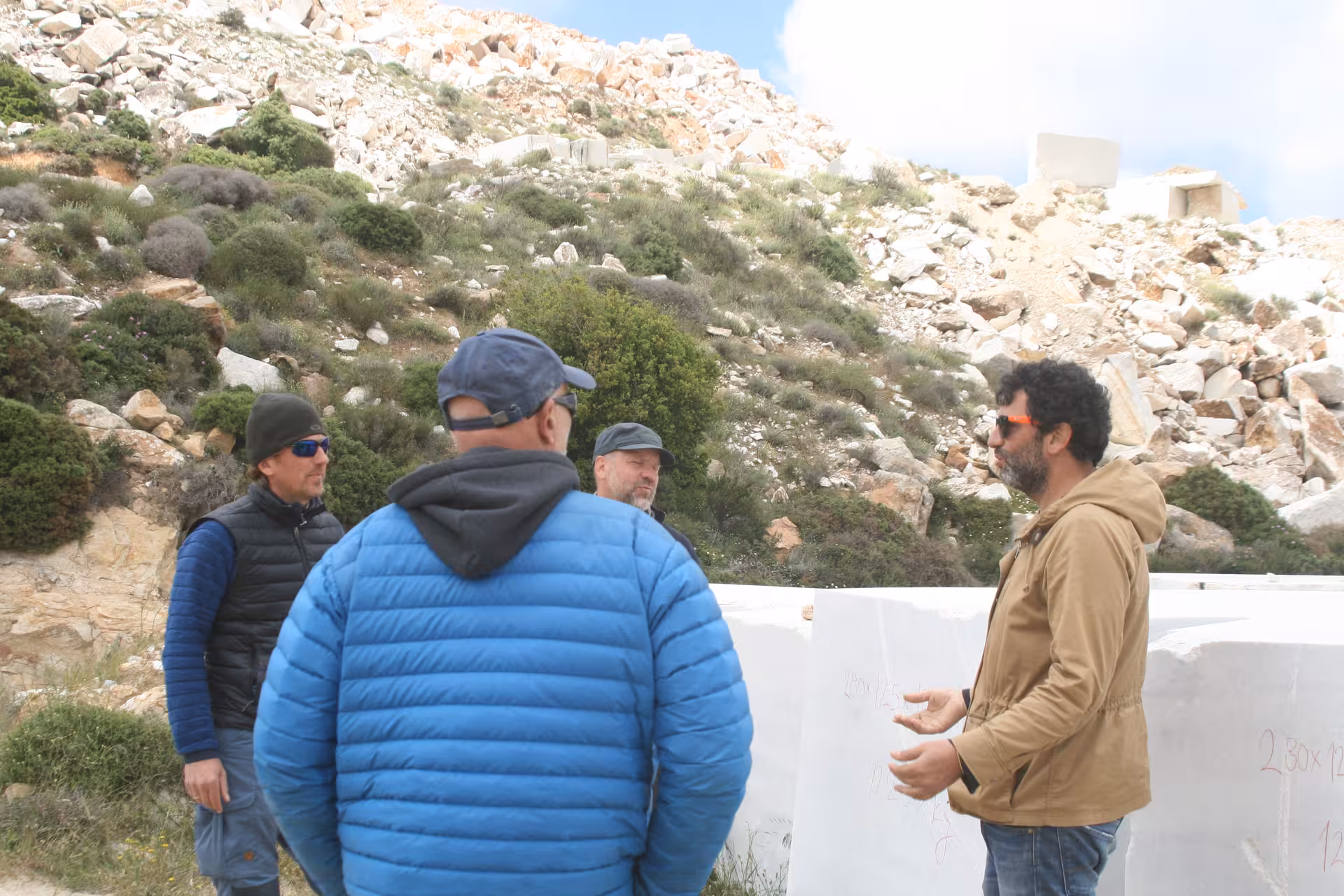 Guide briefing visitors beside massive white marble blocks on Marble World quarry tour, rocky hillside backdrop