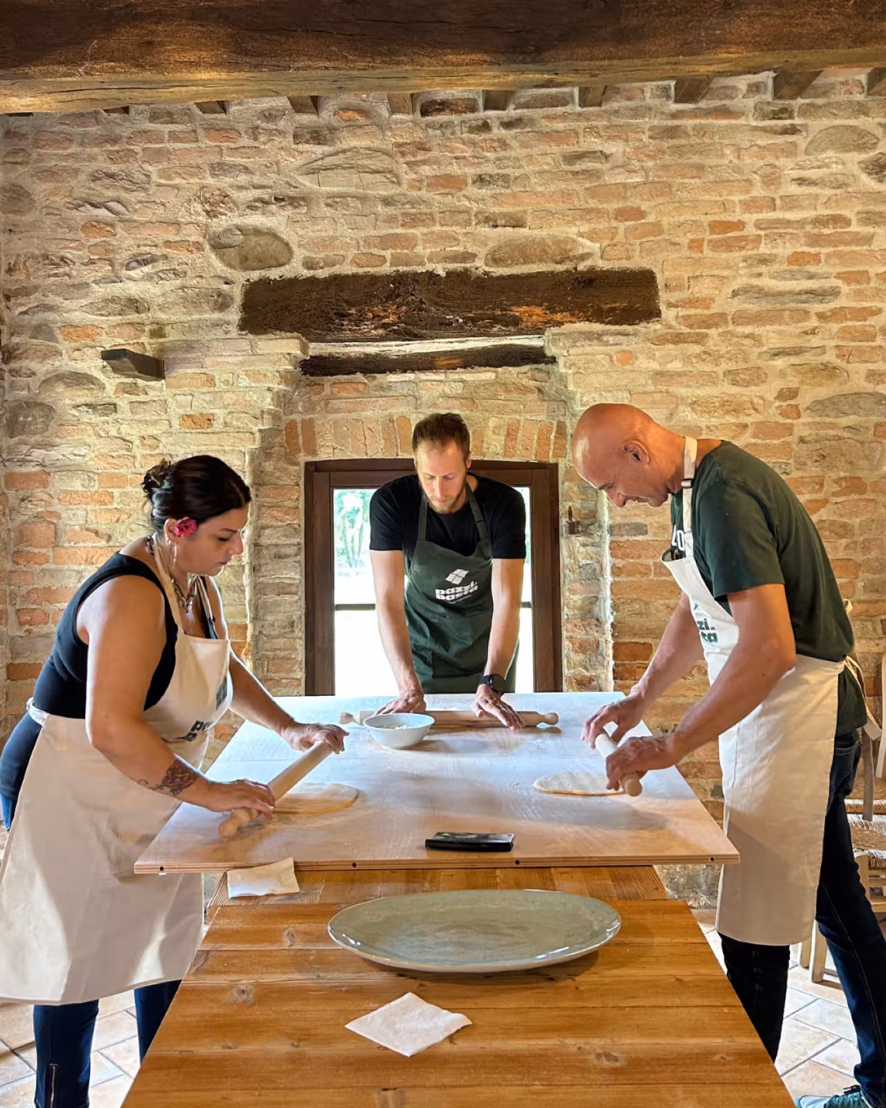 Hands-on Marche pasta workshop in a rustic kitchen, guests rolling fresh dough with wooden pins on a large table
