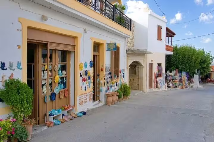 Picturesque street in Margarites village featuring vibrant ceramic art on shop facades and lush greenery.