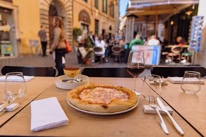 A delicious Margherita pizza with a glass of red wine served at an outdoor table in Rome's vibrant street ambiance.