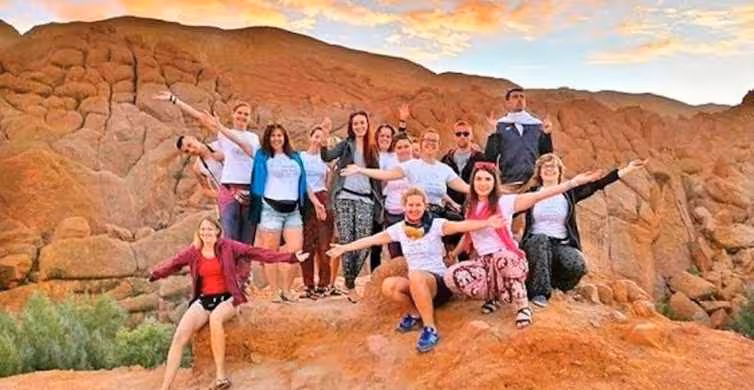 A group of tourists pose joyfully amidst the stunning rock formations of Dades Valley on their Moroccan desert adventure.