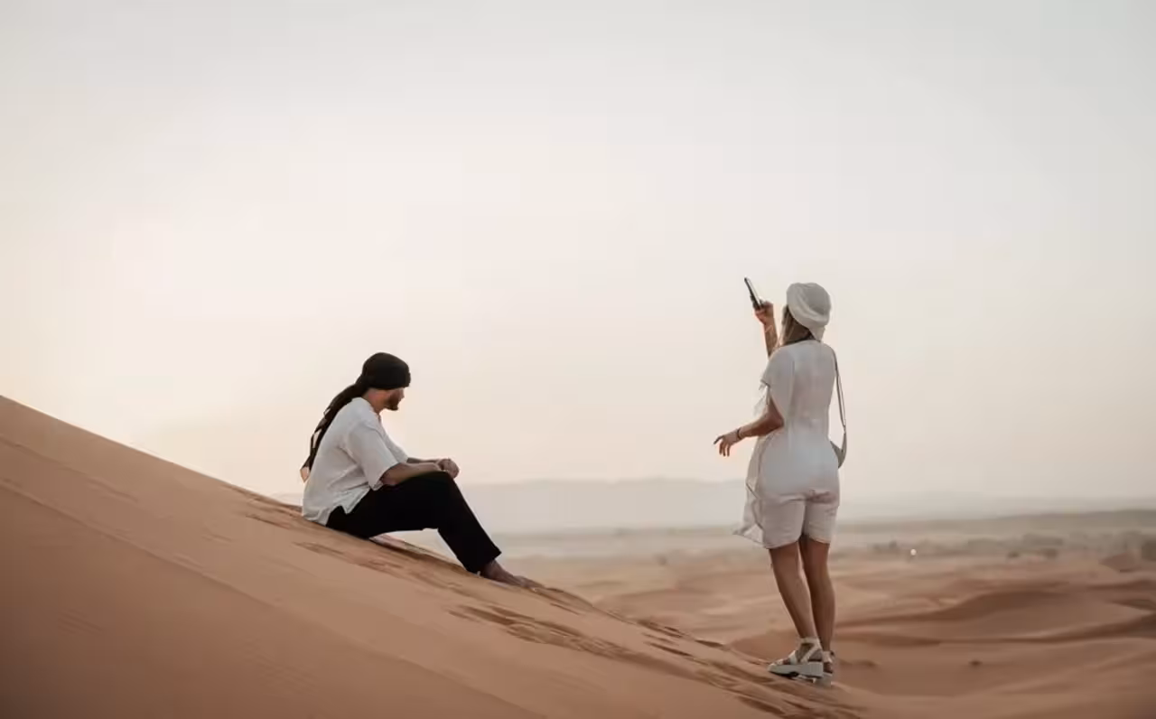 Two travelers enjoy a serene moment on the Merzouga dunes during a 4-day Marrakech to Fez desert tour.