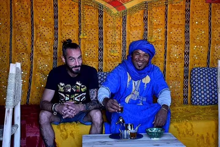 Traveler sharing Moroccan tea with Berber host inside a desert tent on a private 2-day Marrakech to Zagora tour