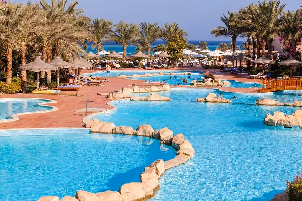 Enjoy luxury at a resort pool surrounded by palm trees in Marsa Alam, Egypt, offering a tropical oasis and ocean views.