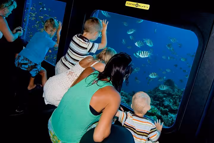 Family viewing colorful fish through Royal Seascope submarine window on Marsa Alam Red Sea cruise with pickup