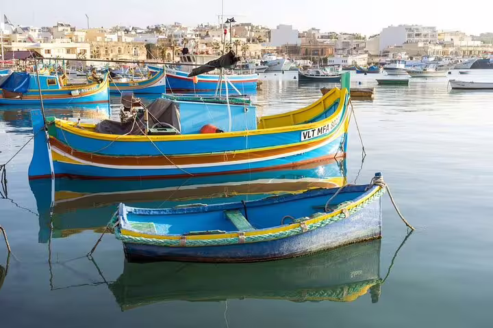 Vibrant traditional Maltese boats docked at Marsaxlokk harbor, showcasing colorful reflections on the calm water.
