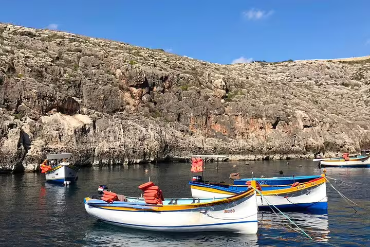 Colorful fishing boats float in the clear waters of Marsaxlokk, backed by rugged, rocky terrain.
