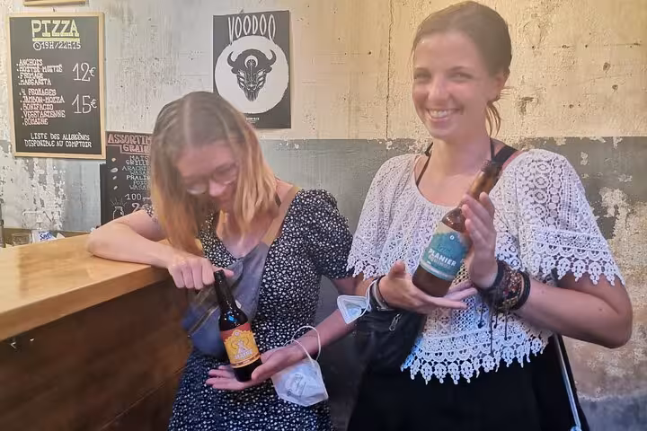 Happy guests show local craft beer bottles during a Marseille beer tasting tour at a trendy bar