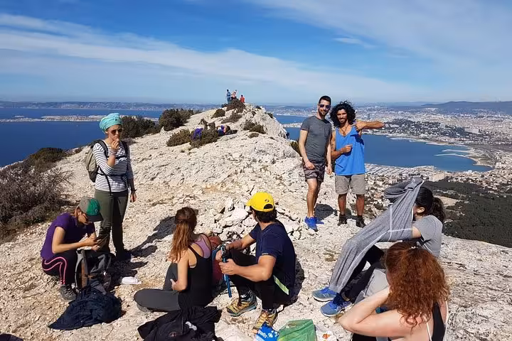 Hikers resting on a rocky summit with sweeping Marseille and Les Calanques coastline views on a guided trek