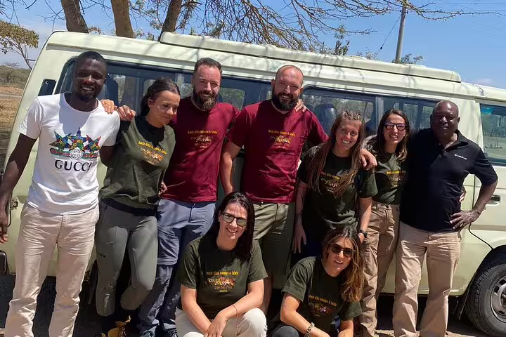 Group of tourists posing with guides in front of a safari jeep, ready for adventure on a 3-day Masai Mara tour.