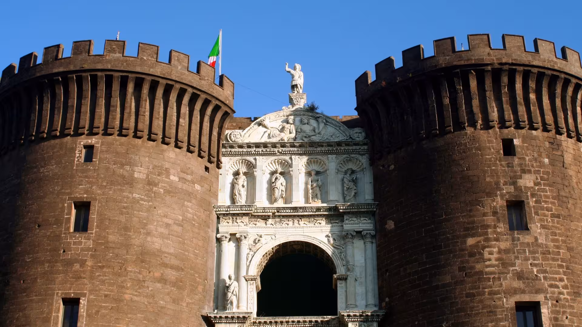 Close-up of Maschio Angioino castle with intricate sculptures under a clear blue sky in Naples, Italy.