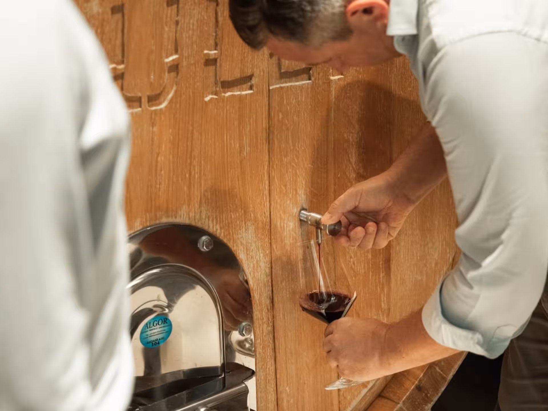 Close-up of a Masseria winery expert pouring red wine from a barrel, highlighting the tasting experience near Taranto.