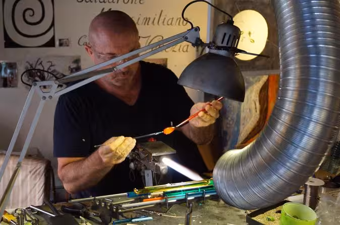 Master artisan demonstrates glassblowing technique in private lesson, crafting vibrant molten glass with precision tools.