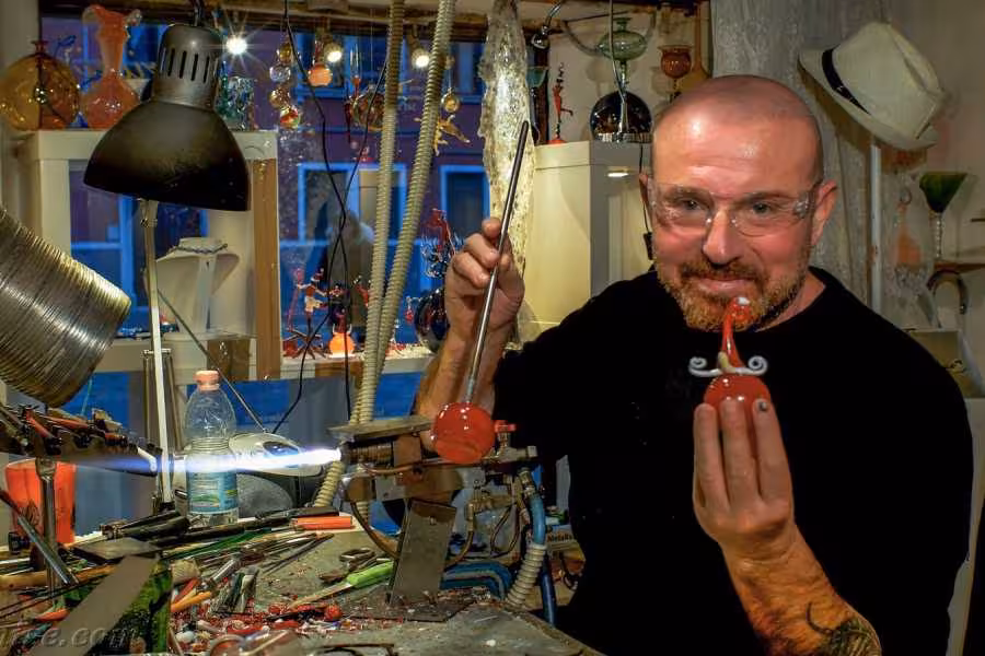 Master artisan demonstrating glassmaking techniques in a vibrant workshop, creating a unique glass piece.