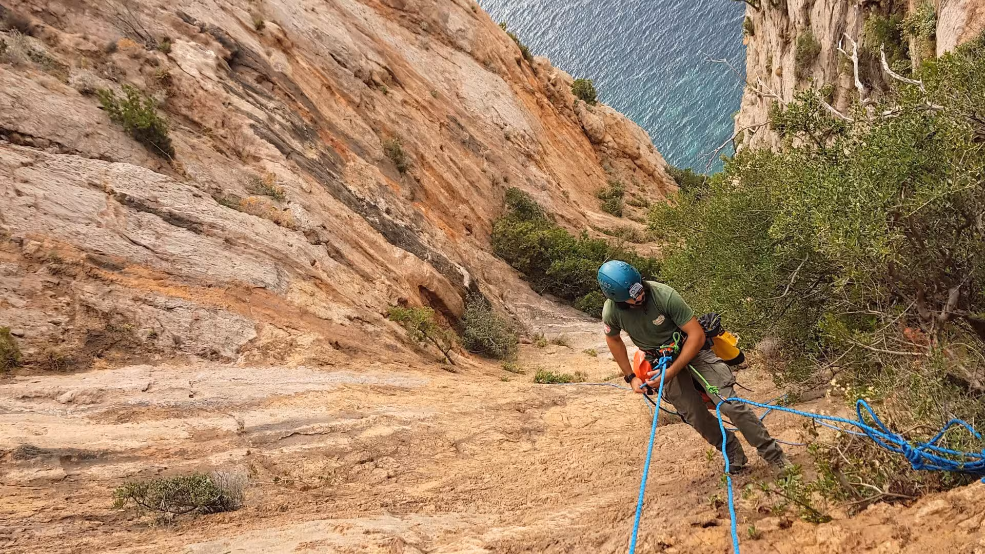 Adventurer descends rocky Masua canyon with ropes, Porto Flavia canal visible, perfect for dry canyoning tours.