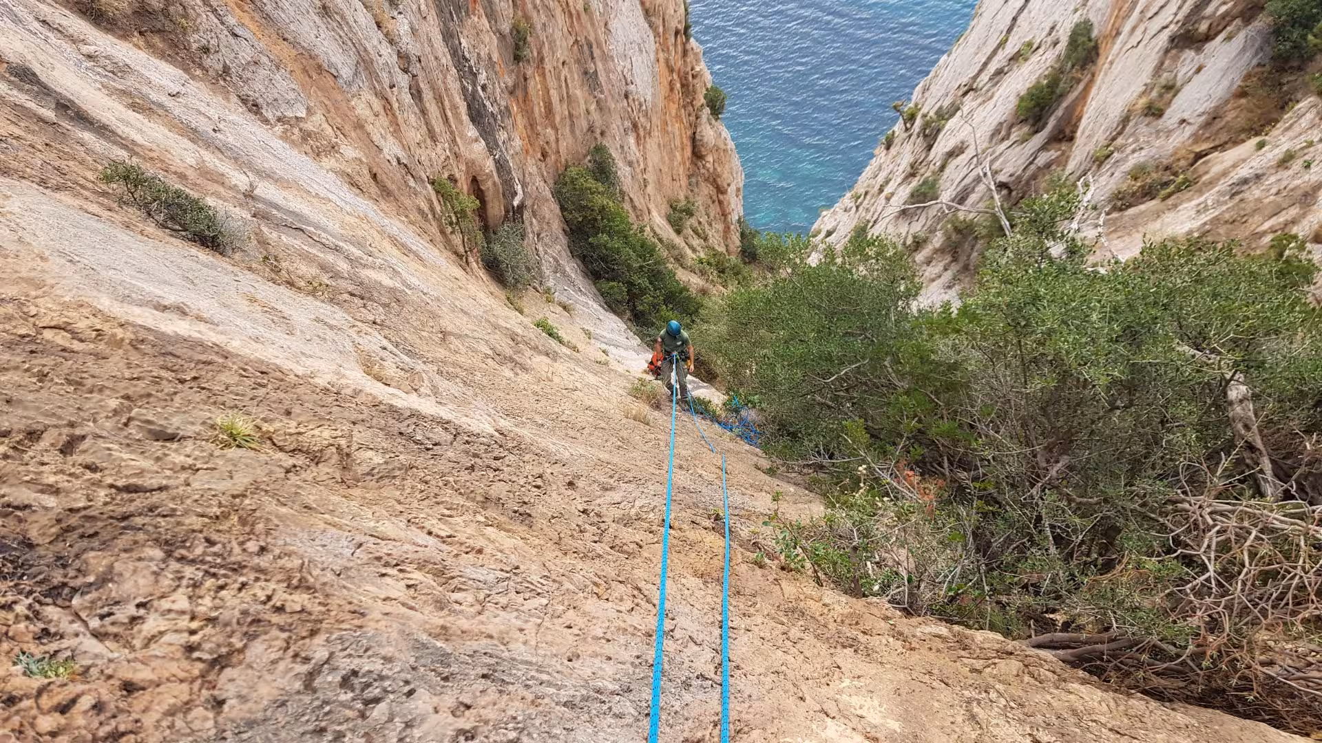 Hiker rappels down steep Masua cliffs with blue ropes, overlooking stunning ocean views in Porto Flavia.