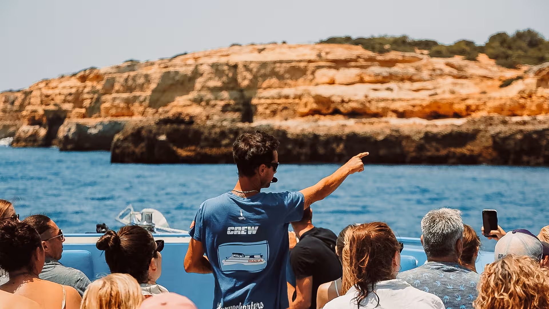 Tour guide points out scenic coastal formations to passengers on the MATRIX boat tour, highlighting Algarve's natural beauty.