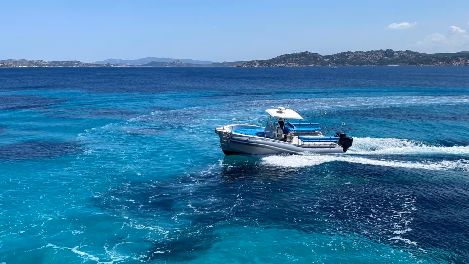 A maxi dinghy sails across the turquoise waters of La Maddalena Archipelago, offering a scenic island tour.