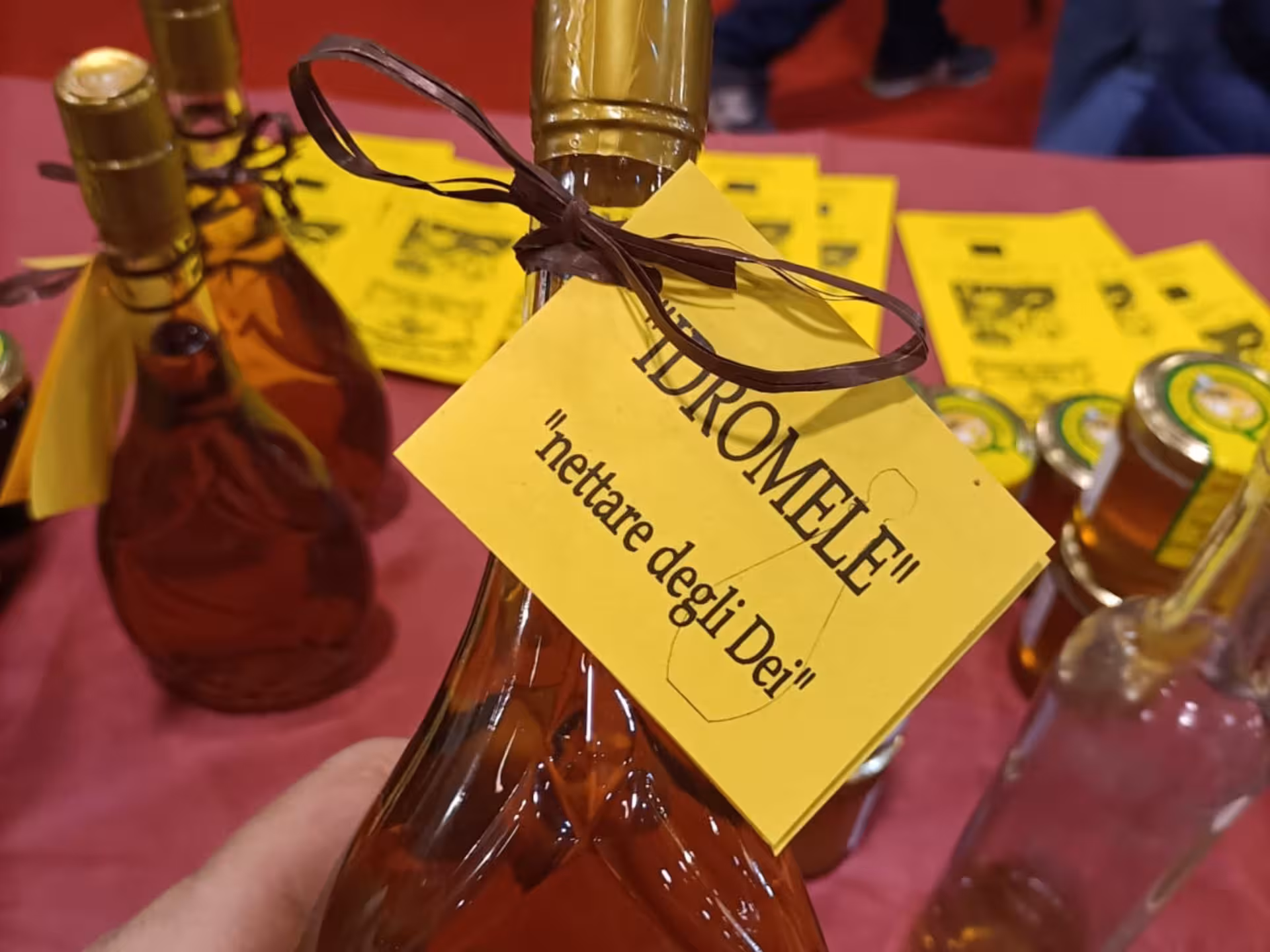 Hand holding a bottle of mead labeled 'nettare degli Dei' at a honey tasting in Monferrato, Italy.