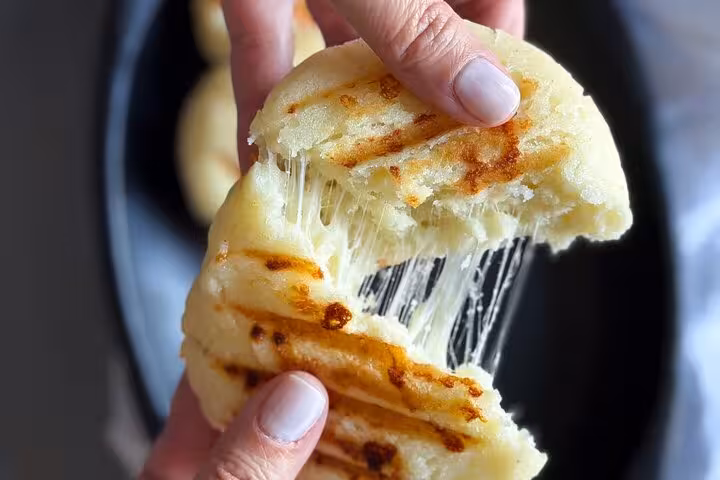 Hands tearing apart a grilled arepa with melted cheese, showcasing Medellín's authentic street food experience.