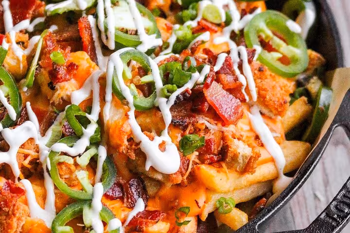 Loaded fries topped with crispy bacon, jalapeños, and drizzled with creamy sauce, ideal for Medellín street food enthusiasts.