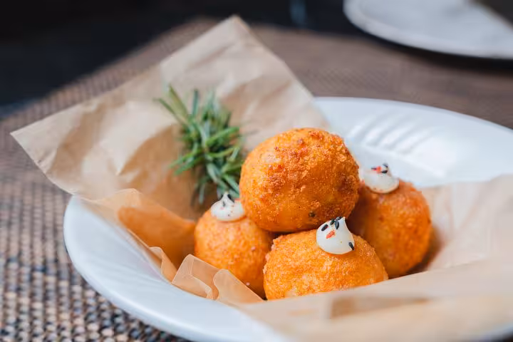 Crispy fried balls garnished with aioli, offering a taste of Medellín's culinary scene in the bustling Laureles district.