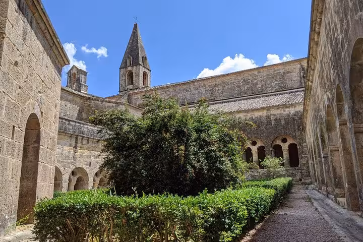 Peaceful courtyard of a medieval church in Provence, featuring stone arches and lush greenery under a clear blue sky.