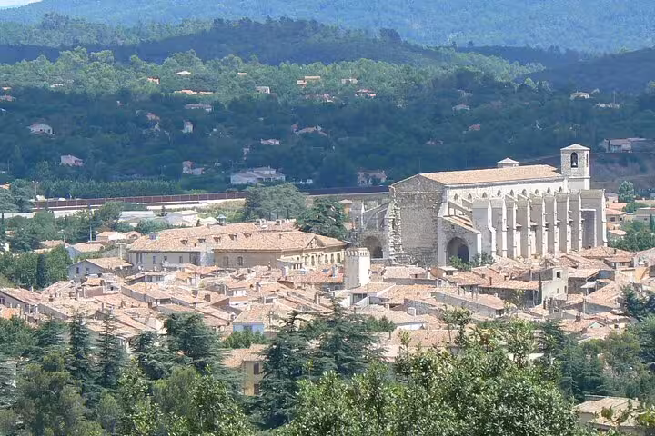 Scenic panorama of a medieval church amidst charming rooftops and verdant hills in the heart of Provence.
