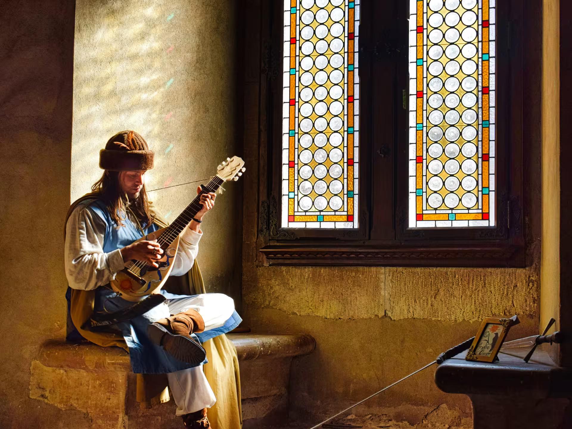 Medieval musician in costume playing lute inside Corvin Castle with colorful stained glass window backdrop