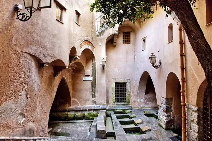 Medieval stone washhouse in Cefalù with arched walls, mossy basins and shaded courtyard on a private tour from Palermo