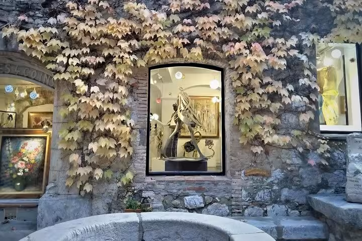 Charming art gallery window in a medieval village adorned with vibrant ivy, showcasing exquisite sculptures and paintings.