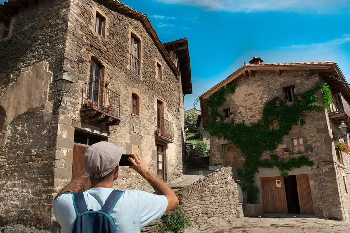 Traveler photographing charming stone buildings in a picturesque medieval village in Catalonia under a clear blue sky.