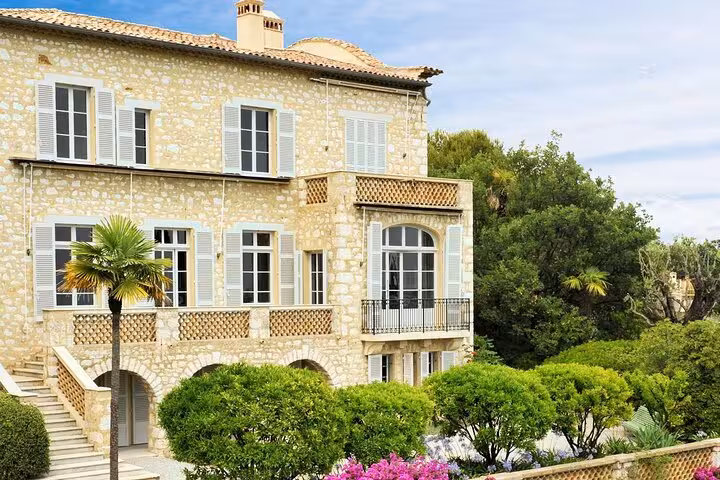 Elegant stone villa surrounded by vibrant gardens and palm trees in a serene medieval village setting.