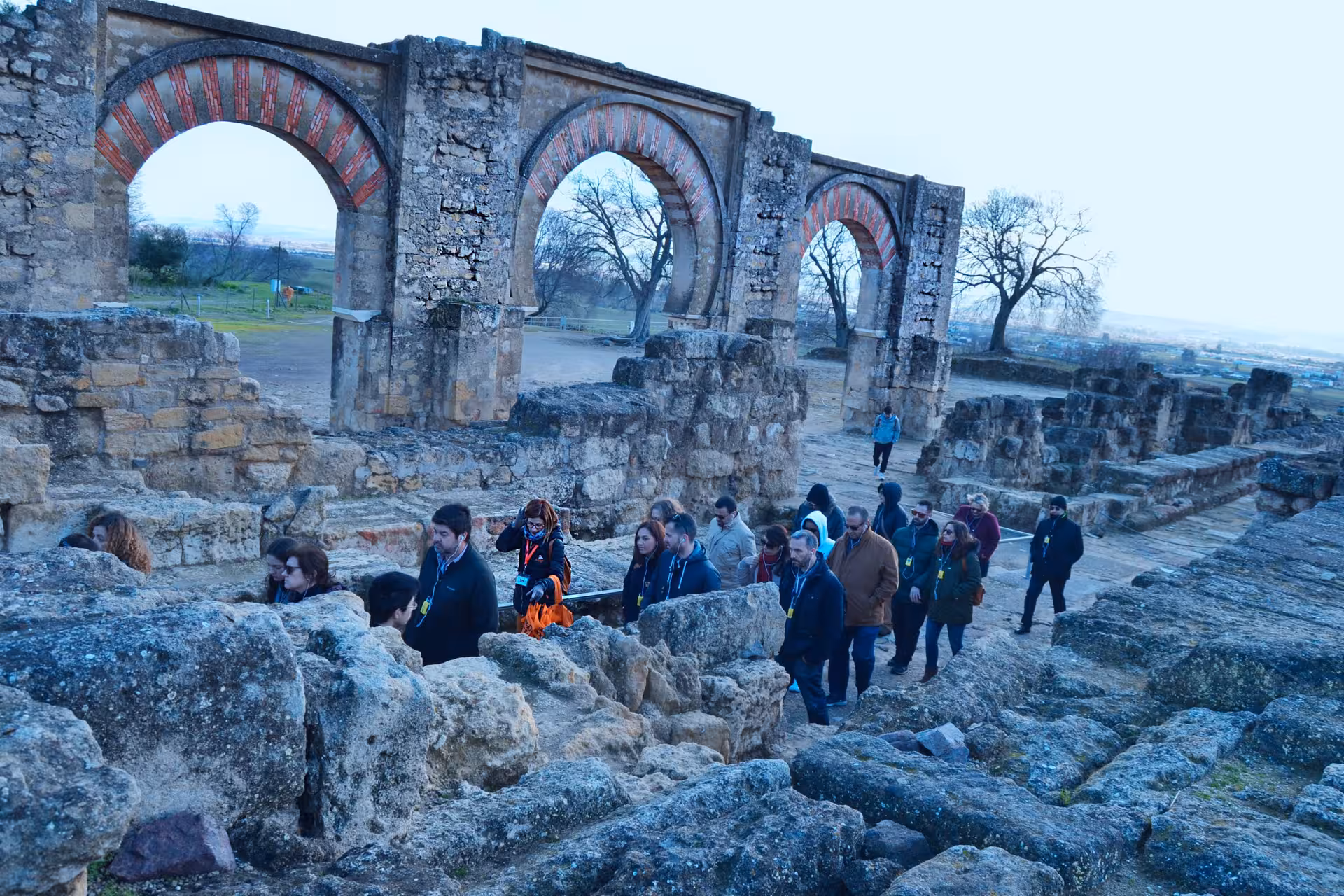 Tour group navigates ancient ruins of Medina Azahara with historical arches in view.
