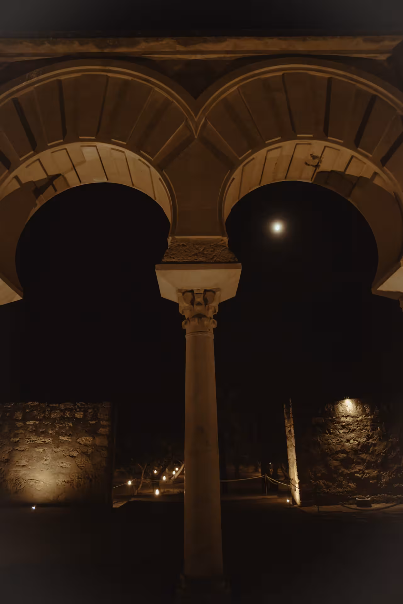 Night view of illuminated arches and columns at Medina Azahara, highlighting historic architecture under a moonlit sky.
