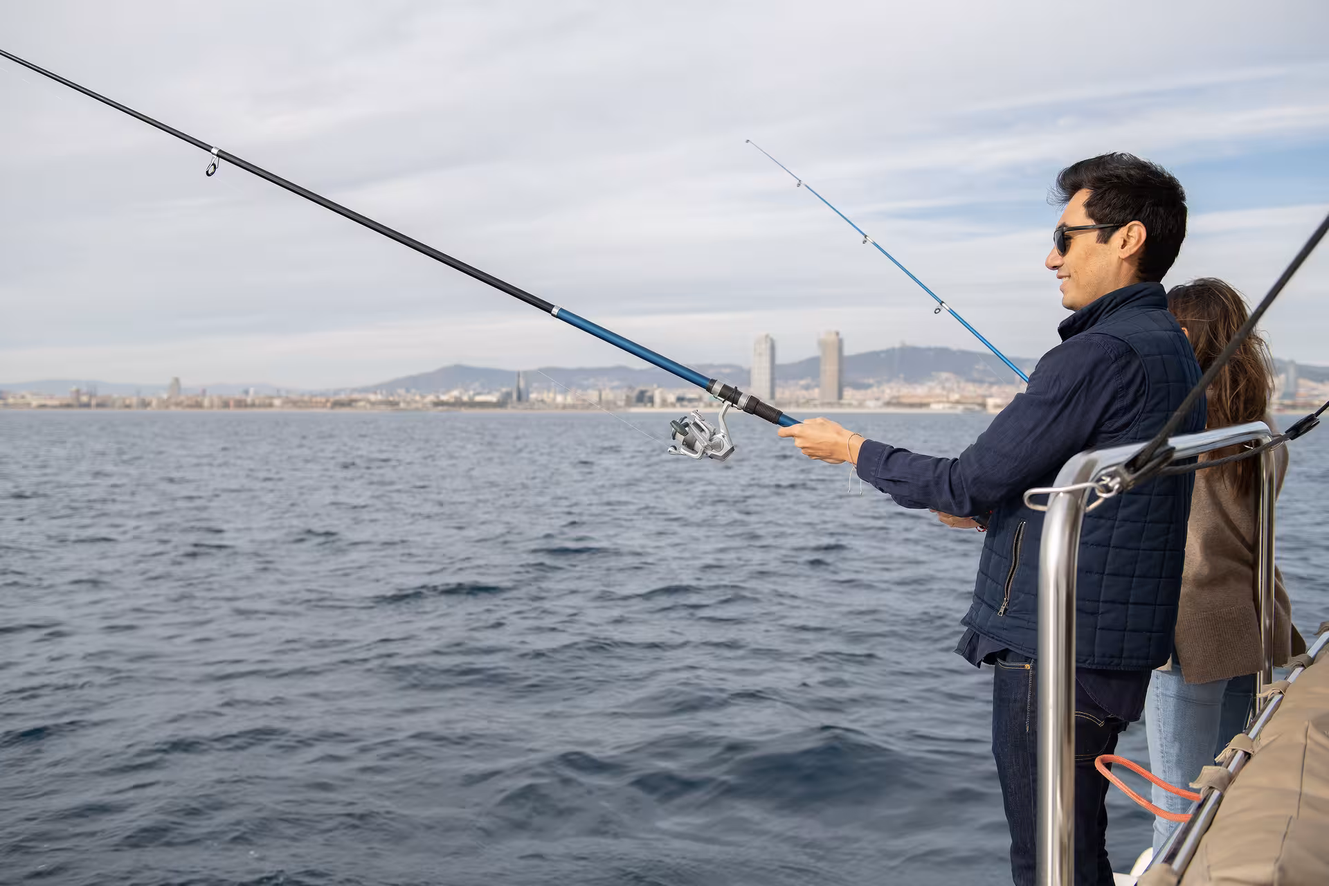 Anglers casting rods from a boat on a Mediterranean sea fishing trip with coastal city skyline in the distance