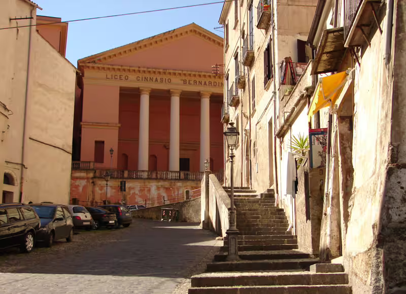 Quiet historic street in Italian hill town leading to Liceo Ginnasio Bernardino classical facade on Mediterranean Passion itinerary