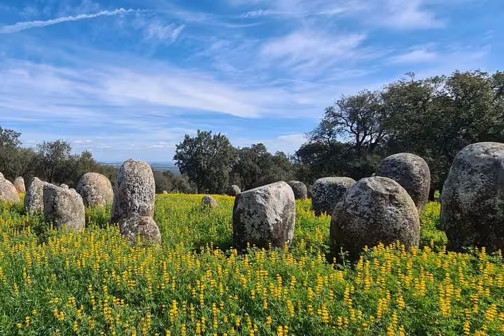 Scenic view of ancient megalithic stones in a vibrant yellow flower field near Évora, Portugal.