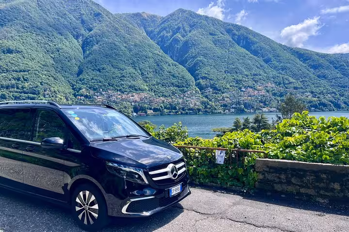 Mercedes van by scenic Lake Como en route from Milan to Courchevel, showcasing lush mountains.