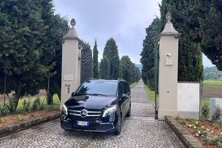 Mercedes van exits gated driveway, highlighting private transfer service from Milan to Courchevel through scenic routes.