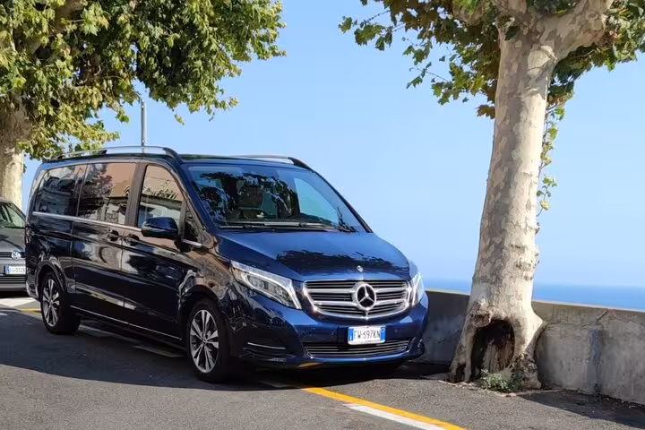 Luxurious blue Mercedes van parked by the scenic Amalfi Coast for private Sorrento to Positano transfers.
