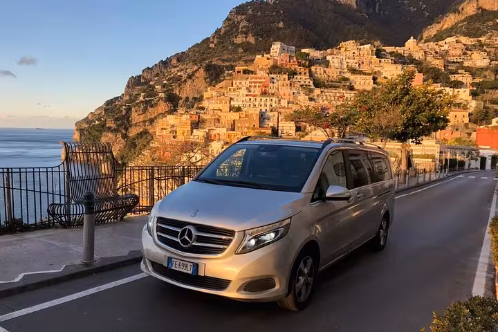 Mercedes van on coastal road with stunning Positano backdrop for private transfer service.