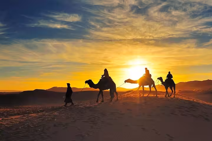 Silhouetted camel caravan at sunset in the Merzouga Desert during a magical 3-day tour from Fes.