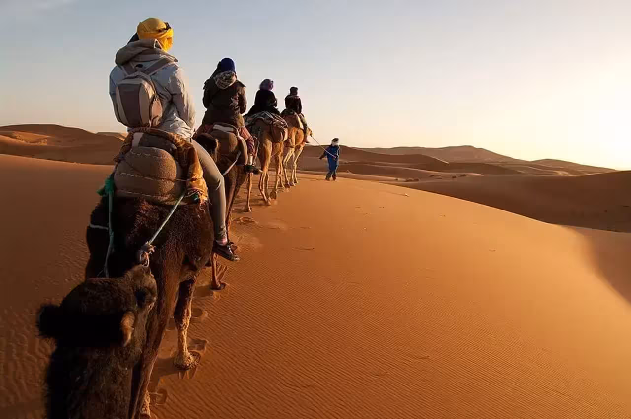 Travelers on camelback trekking through the golden dunes of the Merzouga Desert at sunset during a Marrakech safari tour.