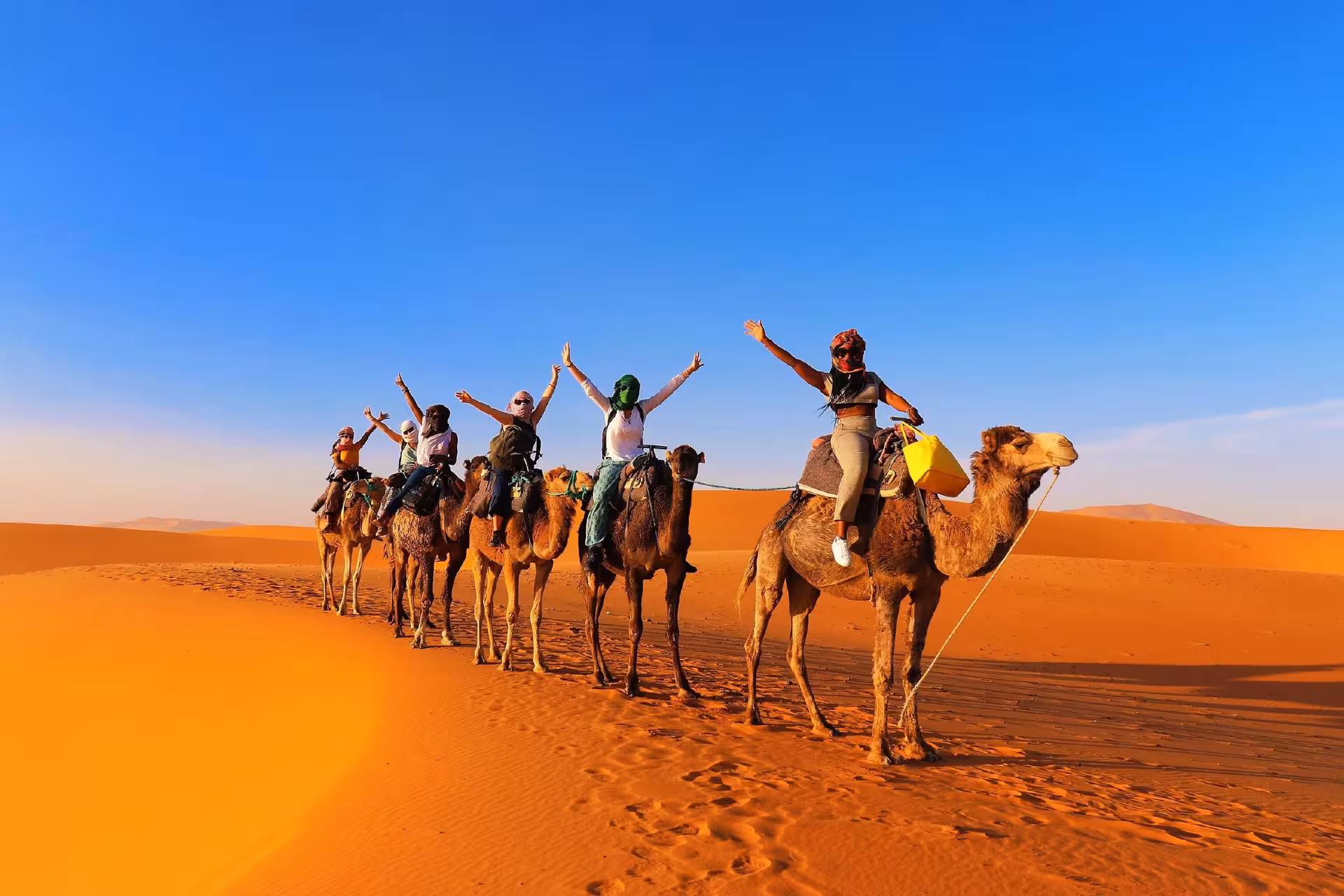 Tourists enjoying a camel ride under a clear blue sky in the stunning Merzouga Sahara desert.