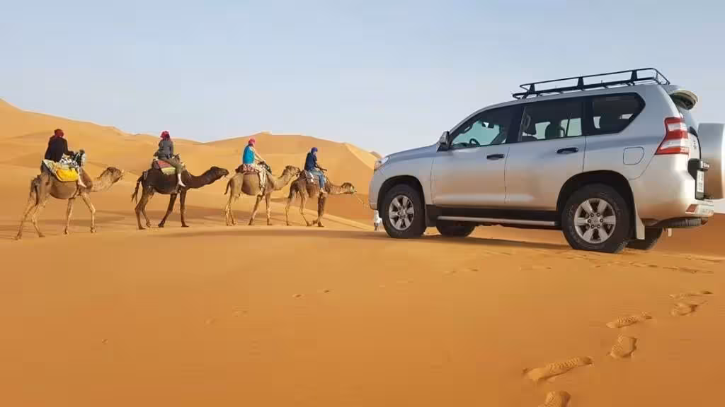 Camel caravan and 4x4 vehicle traverse Merzouga dunes on an adventure tour in Morocco's Sahara Desert.