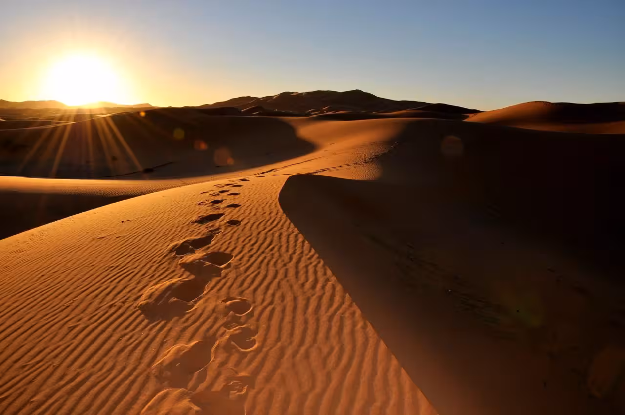 Sunrise over Merzouga Sahara dunes with footprints, part of 2-day desert tour from Marrakech to Fez.