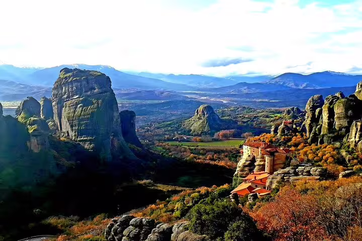 Stunning view of Meteora's rock formations and monasteries from above, showcasing vibrant autumn foliage and mountains.