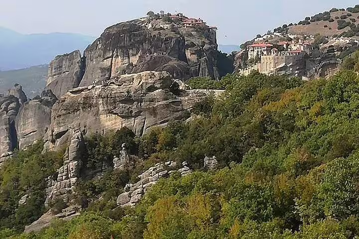 Meteora cliffs and hilltop monasteries above lush forest on full-day tour from Athens including dinner